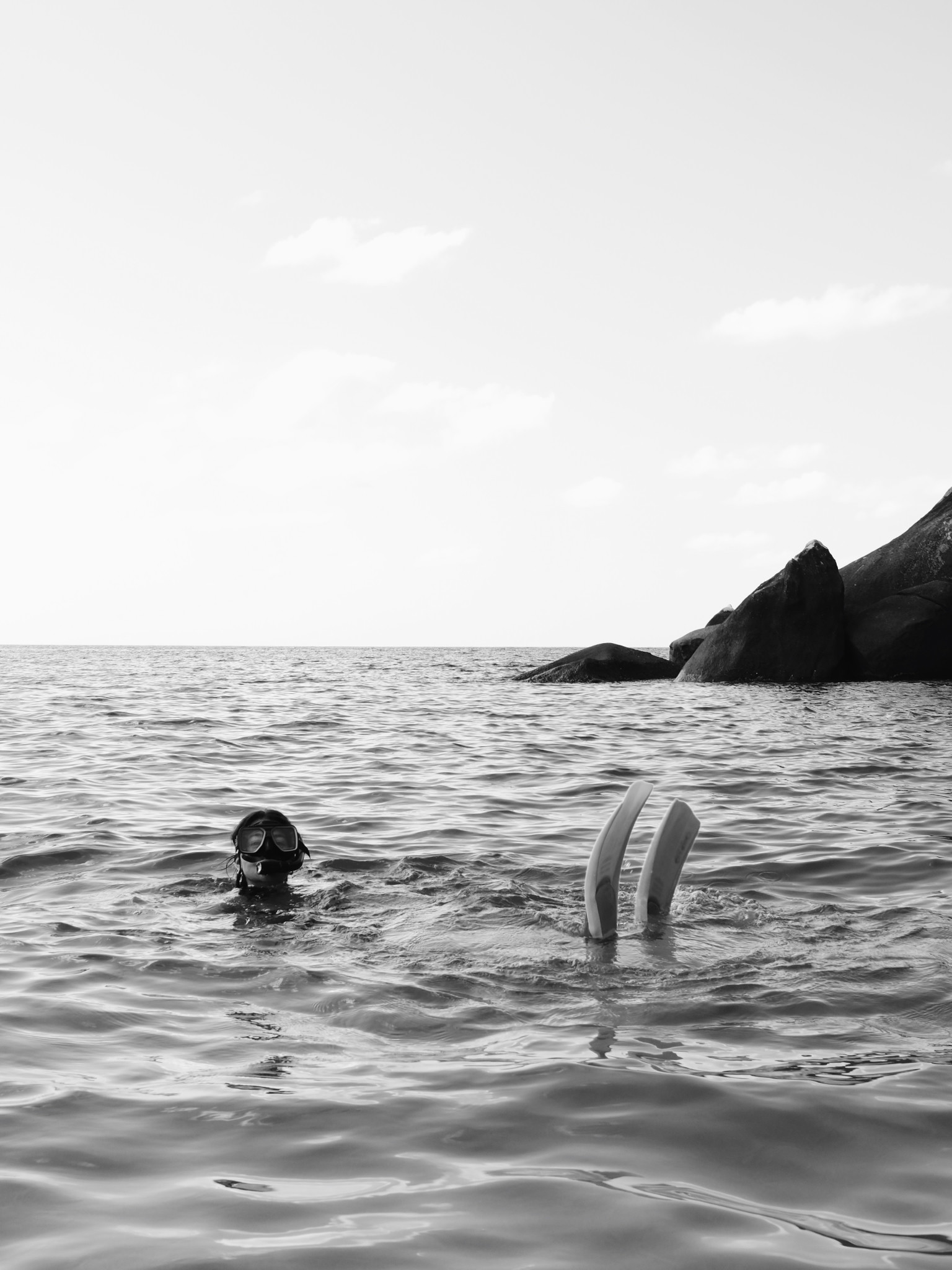 A swimmer and fins in a calm sea, photographed in black and white